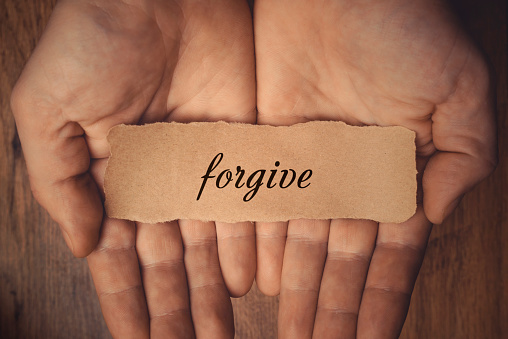 two hands with palms facing up, holding a piece of paper with "forgive" written on it